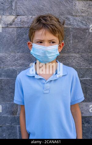 Un ragazzo in una t-shirt blu, indossando una maschera medica su uno sfondo di coronovirus su uno sfondo grigio. Un bambino in una maschera. Foto Stock