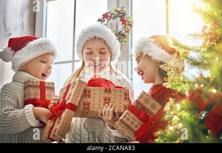 Buon Natale e buone feste! Allegri e simpatici regali di apertura per i bambini. I bambini si divertono vicino all'albero al mattino. Famiglia amorevole con regali in roo Foto Stock