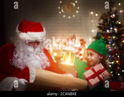 Сute elfo aiuta Babbo Natale a leggere la lista dei desideri Foto Stock
