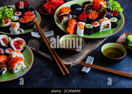 Set di sushi con vari sashimi, sushi roll e tè serviti su ardesia di pietra Foto Stock