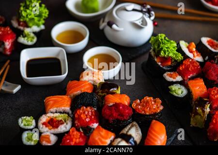 Set di sushi con vari sashimi, sushi roll e tè serviti su ardesia di pietra Foto Stock