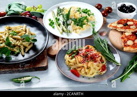 Varietà di pasta vegana preparata in casa, pizza e spuntini su sfondo grigio. Cucina italiana. Foto Stock