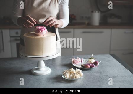 Donna che fa la torta decorando con rose di fiore che rimangono sul tavolo da cucina da vicino a casa. Giorno del matrimonio. Messa a fuoco selettiva. Foto Stock