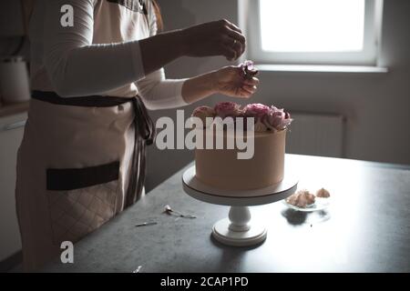 Donna che fa la torta decorando con rose di fiore che rimangono sul tavolo da cucina da vicino a casa. Giorno del matrimonio. Messa a fuoco selettiva. Foto Stock