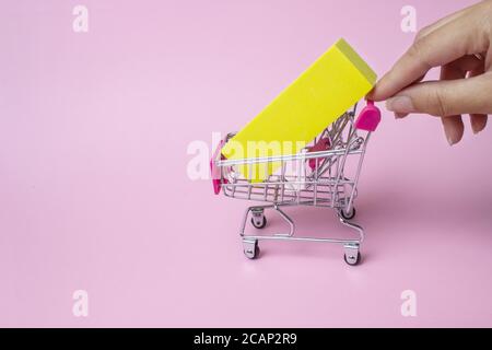 Primo piano della mano femminile spinge il carrello giocattolo in metallo con manico in plastica rossa e scatola gialla all'interno su sfondo rosa. Grandi sconti e sconti in Gro Foto Stock