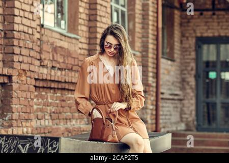 Bella giovane donna in abito corto seduta sulla panchina e alla ricerca di un someting in borsa Foto Stock