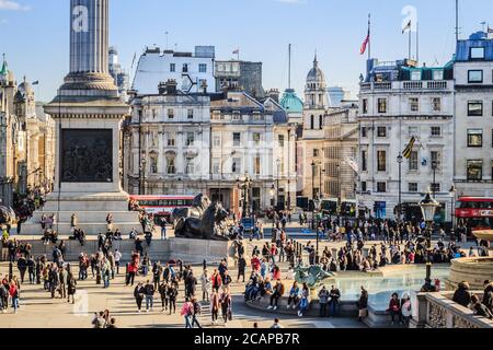 Trafalgar Square, Londra, con persone che si trovano in giro per la città e che camminano nella piazza. Vista della strada dalla Galleria Nazionale. Foto Stock