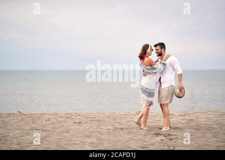 giovane adulto caucasico coppia abbracciare, guardando l'un l'altro, in piedi nudi in spiaggia di sabbia Foto Stock