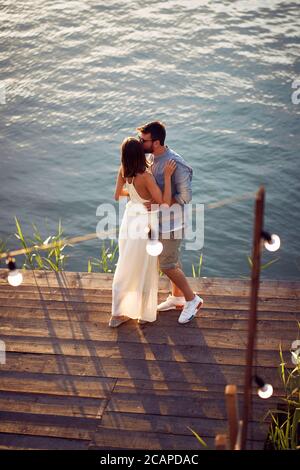 giovane coppia in piedi abbracciata su piattaforma di legno vicino al mare, baciando Foto Stock