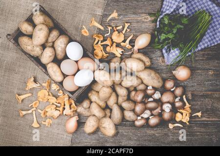 Patate, funghi, uova, parslex, erba cipollina e cipolle su un tavolo di wodden con burlap Foto Stock