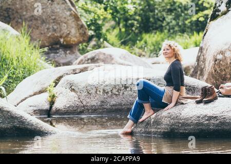 Donna con zaino che riposa mentre camminando nella valle del fiume. Eco-turismo con bastoni nordici Foto Stock