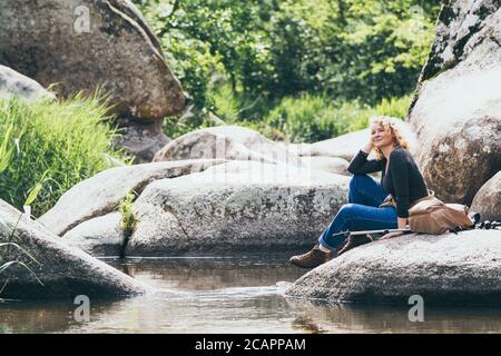 Donna con zaino che riposa mentre camminando nella valle del fiume. Eco-turismo con bastoni nordici Foto Stock