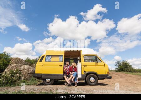 Giovane coppia dell'Europa orientale che viaggia in un camper giallo attraverso la campagna. Campeggio off-grid auto-costruito in campeggio nella natura selvaggia. Foto Stock