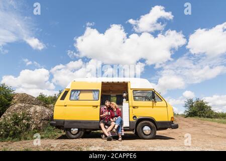 Giovane coppia dell'Europa orientale che viaggia in un camper giallo attraverso la campagna. Campeggio off-grid auto-costruito in campeggio nella natura selvaggia. Foto Stock