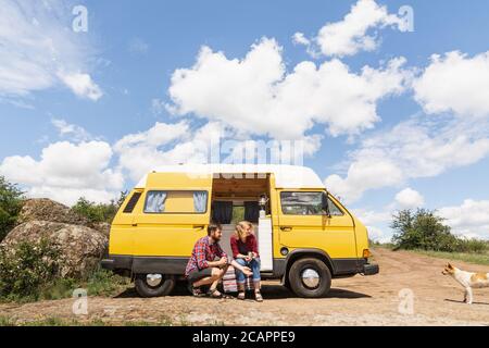 Giovane coppia dell'Europa orientale che viaggia in un camper giallo attraverso la campagna. Campeggio off-grid auto-costruito in campeggio nella natura selvaggia. Foto Stock