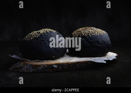 hamburger nero rotola su uno sfondo scuro con un primo piano del lato orizzontalmente Foto Stock