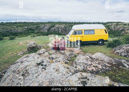 Giovane coppia dell'Europa orientale che viaggia in un camper giallo attraverso la campagna. Campeggio off-grid auto-costruito in campeggio nella natura selvaggia. Foto Stock