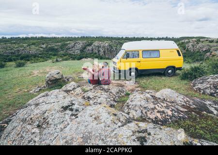 Giovane coppia dell'Europa orientale che viaggia in un camper giallo attraverso la campagna. Campeggio off-grid auto-costruito in campeggio nella natura selvaggia. Foto Stock