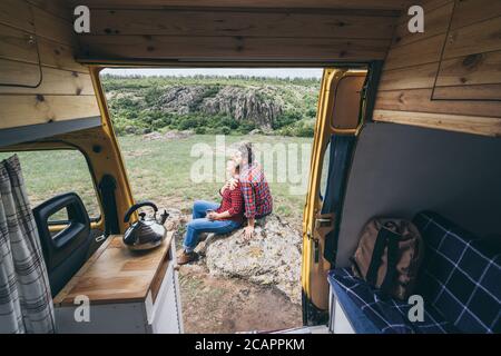 Giovane coppia dell'Europa orientale che viaggia in un camper giallo attraverso la campagna. Campeggio off-grid auto-costruito in campeggio nella natura selvaggia. Foto Stock