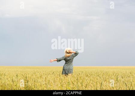 Donna in cappello di paglia che cammina attraverso il campo di segale sopra giorno d'estate Foto Stock