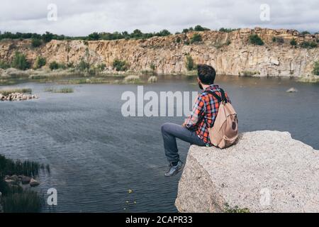 Uomo con zaino escursioni in montagna. Si erge sul bordo della scogliera e si affaccia sul canyon roccioso Foto Stock