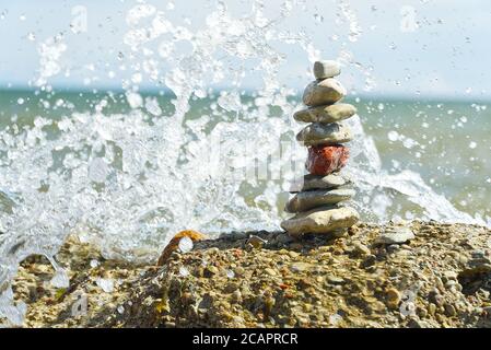 torre in pietra sulla spiaggia rocciosa con spruzzi d'onda. fuoco morbido ciottoli ovali uno su un altro gruppo di make up. Foto Stock