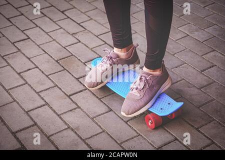 Teenage Girl in Sprurt Shoes è in piedi su un piccolo skateboard di Pennyboard sul sentiero in città, attività di lwisure in ambiente urbano Foto Stock