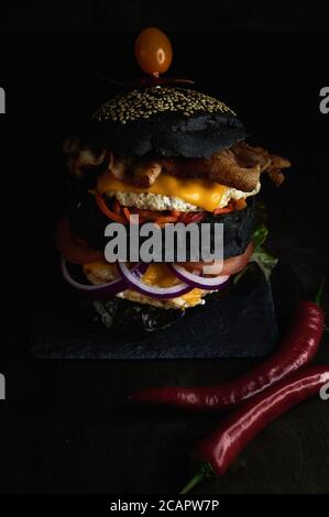 Hamburger nero cipolle rosse e pomodori su una tavola di pietra vicino rosso piccante Foto Stock