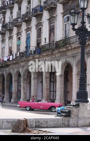 Scena di strada a l'Avana, Cuba, con auto rosa vintage parcheggiata e lavaggio appeso da un edificio in stile coloniale Foto Stock