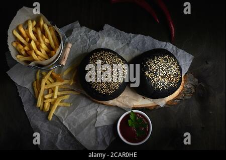 panini neri con patatine fritte al sesamo in un secchio sopra uno sfondo scuro Foto Stock