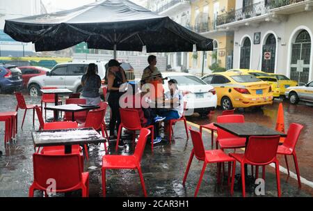 La gente si accoccolò al riparo sotto la tettoia di un bar da una pioggia torrenziale a Panama City, America Centrale Foto Stock