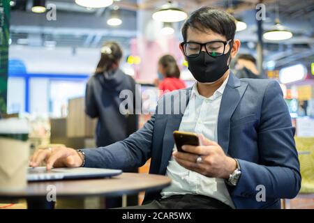 Gli uomini d'affari asiatici stanno parlando al telefono e usando la nota libro per il lavoro, indossa la maschera per proteggere il coronavirus Foto Stock