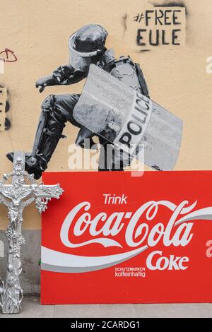 Amburgo, Germania, 23 marzo 2019 - graffiti murales sconvolgenti in città: Un poliziotto che si stanca su un crocifisso, con un annuncio di Coca-Cola accanto ad esso. Foto Stock