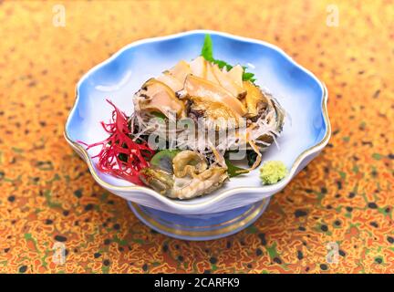 Sashimi crudi alta cucina giapponese di Awabi fresco abalone in un piatto con alghe rosse Gracilaria, foglie di shiso e julienne di rafano daikon A. Foto Stock