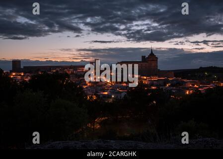 Paesaggio della città illuminata di Uclés con il monastero e il castello in cima alla collina al tramonto, Cuenca, Castilla la Mancha, Spagna Foto Stock