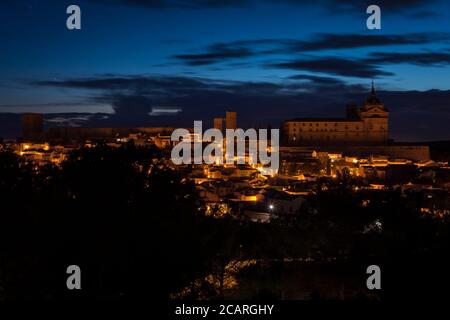 Paesaggio urbano della città illuminata di Uclés con il monastero e il castello in cima alla collina di notte, Cuenca, Castilla la Mancha, Spagna Foto Stock
