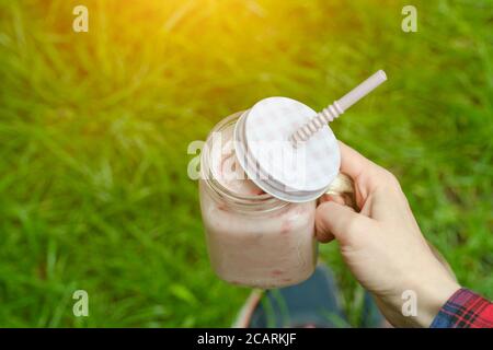 Frullati alla fragola in mano e sneakers su uno sfondo di erba verde Foto Stock