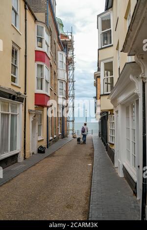 Uomo che cammina con i suoi due cani su un guinzaglio giù un vicolo verso la spiaggia nella città balneare di Cromer sulla costa nord del Norfolk Foto Stock