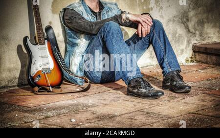 uomo e chitarra elettrica appoggiati su un muro di grunge Foto Stock