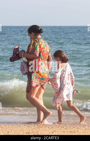 Punta Umbria, Huelva, Spagna - 7 agosto 2020: Madre e figlia camminano vicino alla spiaggia indossando maschere protettive o mediche. Nuovo normale in Spa Foto Stock