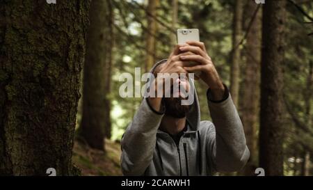 Teenager testando nella foresta con un telefono in mano rompe il segnale, sottolineato giovane uomo con problemi di segnale Foto Stock