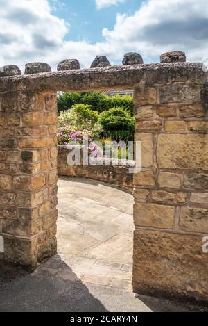Muro in pietra con arco in pietra che conduce ad un giardino Foto Stock