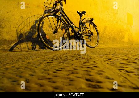 bicicletta appoggiata a un muro sotto una luce gialla a. notte Foto Stock