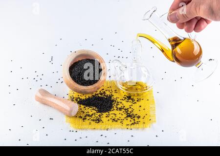 Semi di cumino nero e olio essenziale con ciotola e pala o cucchiaio di legno. Nigella Sativa in bottiglia di vetro. Medicina di erbe organica per molte malattie. Foto Stock