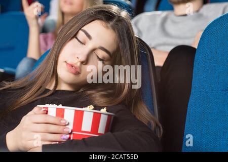 Fare un pisolino. Primo piano di una splendida giovane donna che dorme tenendo il suo secchio di popcorn al cinema Foto Stock
