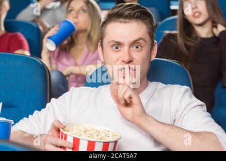 Stai zitto! Ripresa di un giovane infastidito che fa un gesto frugante guardando con rabbia la fotocamera al cinema Foto Stock