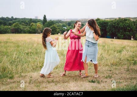 Tre suore caucasiche adulte giocano e si divertono sul campo. Una famiglia di tre giovani donne ridono e trascorrono il tempo estivo in natura. Felice Foto Stock