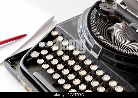 una vecchia macchina da scrivere nera accanto a un foglio di carta bianco con una penna rossa. Giornalismo e strumenti di scrittura. Narrazione e attività creative Foto Stock