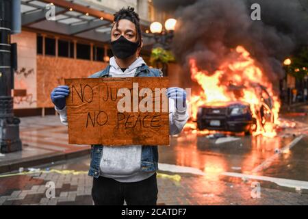 Seattle, USA 30 maggio 2020: Un attivista con un cartello NO JUSTICE NO PEACE, mentre un'auto della polizia brucia sullo sfondo a Westlake. Foto Stock