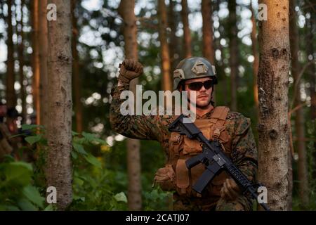 il soldato moderno della guerra sta mostrando i segnali tattici della mano per dare silenziosamente ordini e i generatori per l'ambiente della foresta della squadra Foto Stock